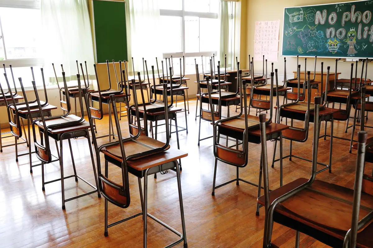 An empty Japanese elementary school classroom with every chair lifted upside down onto a desk, leaving the wooden floor clear
