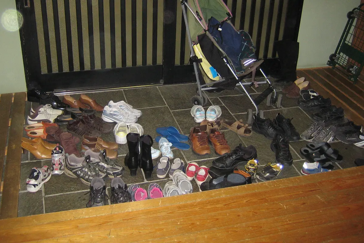 Rows of shoes left on the tiled floor of a Japanese entrance hall, with a raised wooden step marking where the indoor floor begins
