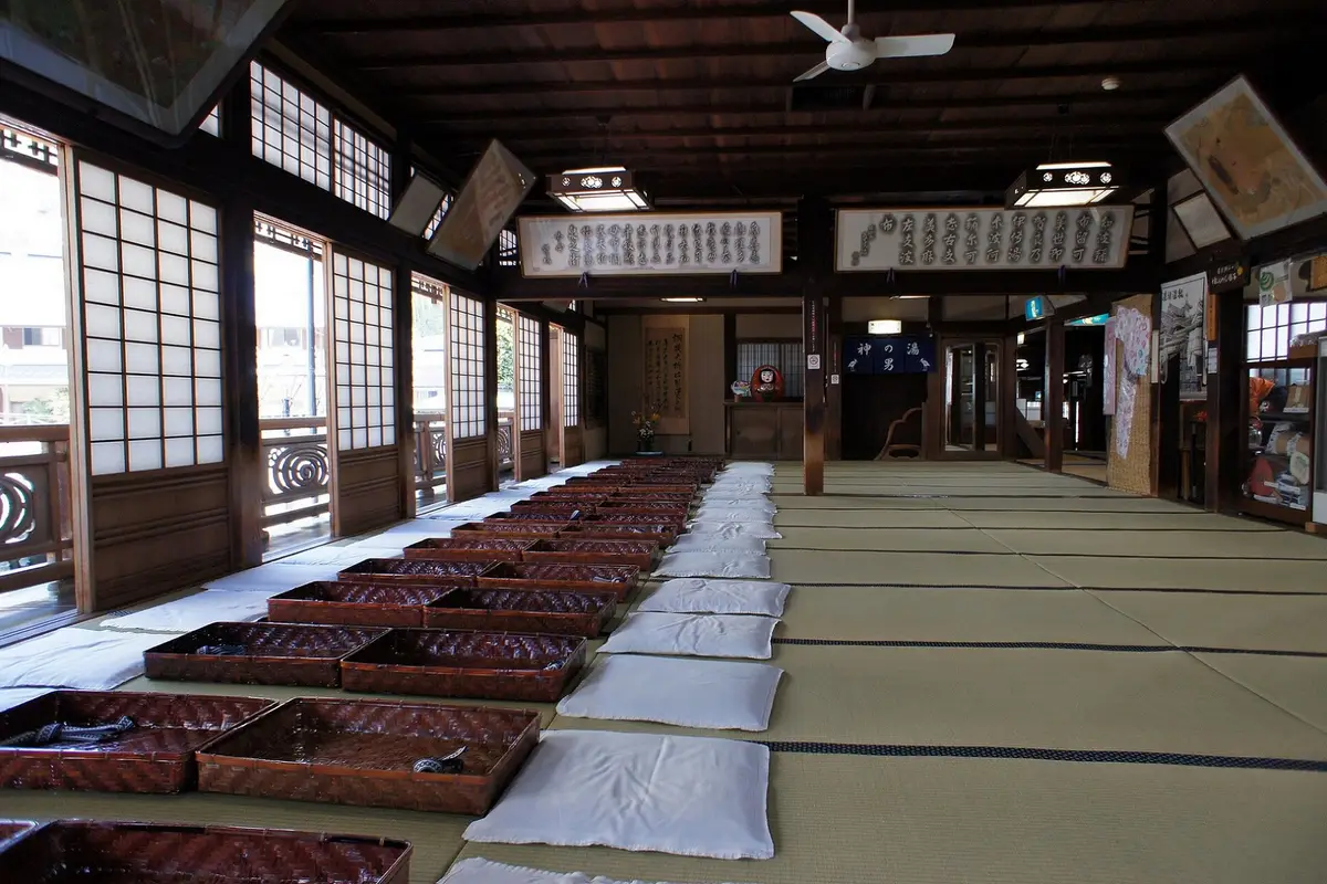 The second-floor tatami rest room of the Dogo Onsen Honkan, with white cushions and woven baskets laid out in rows beside the shoji windows