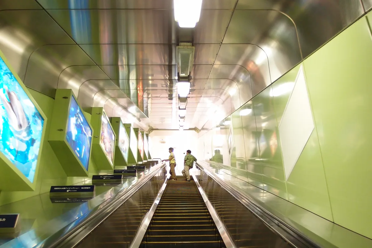 Interior of the Enoshima Escar, an enclosed outdoor escalator with illuminated ocean-themed panels along the tunnel