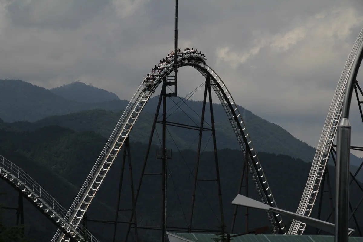 A Fujiyama roller coaster track running alongside a forested hillside at Fuji-Q Highland