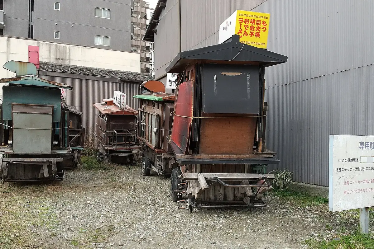 Carretti di legno dei chioschi yatai parcheggiati uno accanto all'altro in uno spiazzo di ghiaia a Fukuoka, di giorno