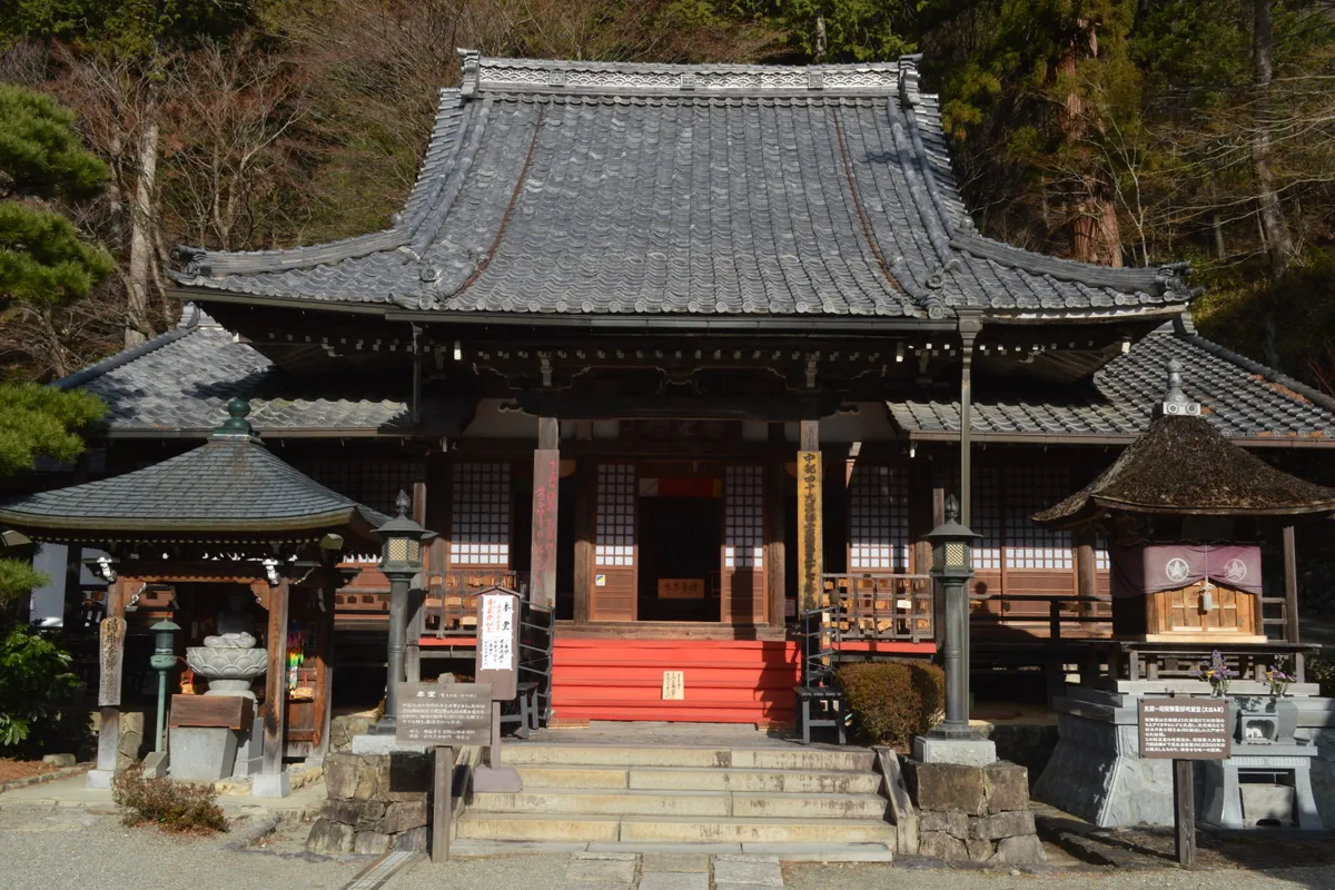 The main hall of Onsenji Temple, with stone lanterns and a short flight of steps in front, on the hillside above the Gero Onsen hot spring town