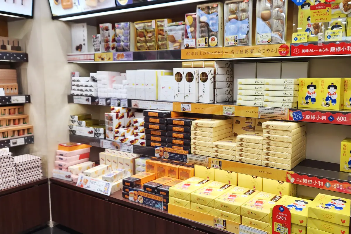 Shelves of boxed Nagoya sweets at a station omiyage counter, with a small price tag under each stack