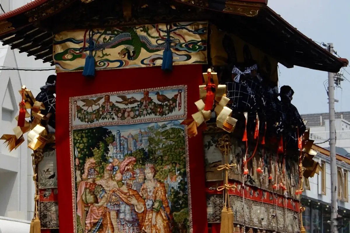A large woven tapestry hanging on the front of a Gion Matsuri float beneath its gilded roof