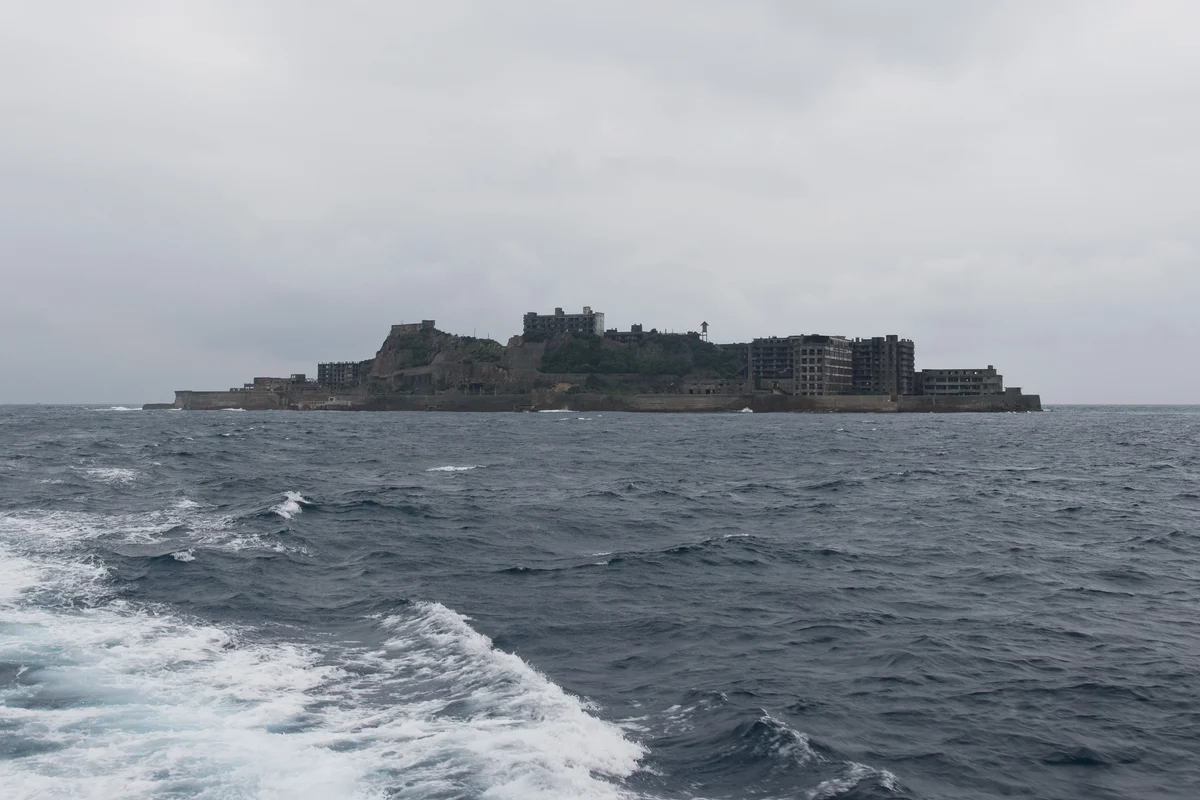Gunkanjima seen from a departing tour boat's wake, its ruined concrete apartment blocks forming the island's battleship silhouette