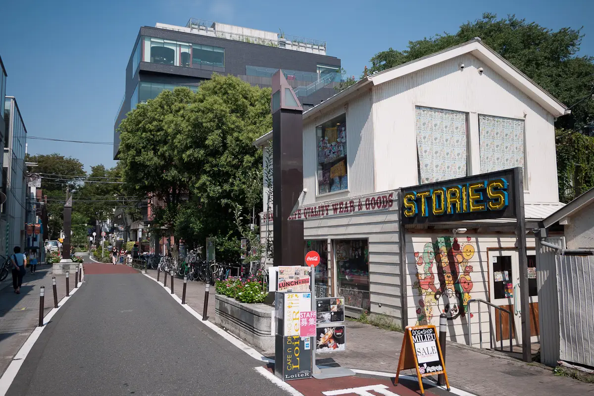 An independent shop with a painted mural on Cat Street in Harajuku, beside a wide, near-empty lane under a blue sky