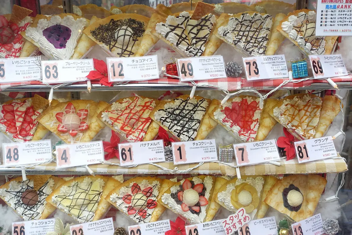 A glass display case of crepe samples outside a shop on Takeshita Street in Harajuku, each one numbered and priced