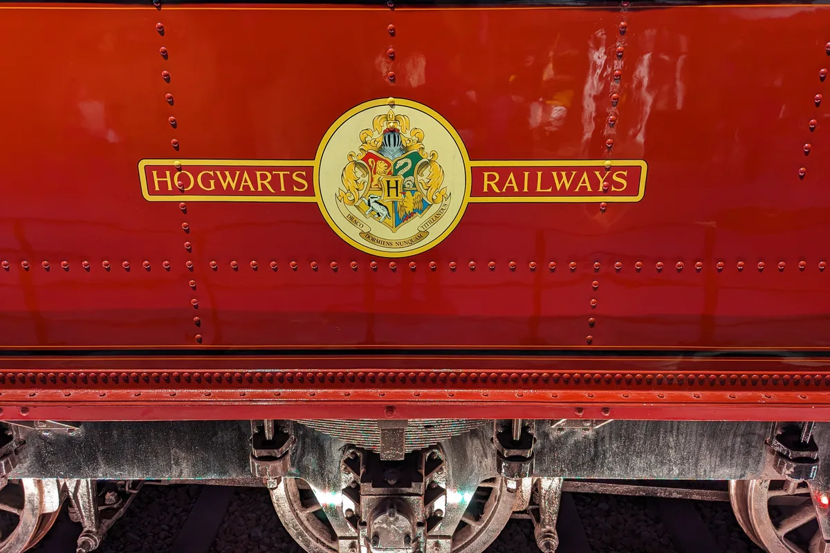 A close-up of the red Hogwarts Express carriage, showing the gold Hogwarts Railways crest riveted onto its side