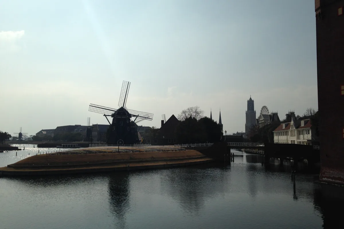 A canal lined with Dutch-style brick buildings and a windmill under a blue sky at Huis Ten Bosch
