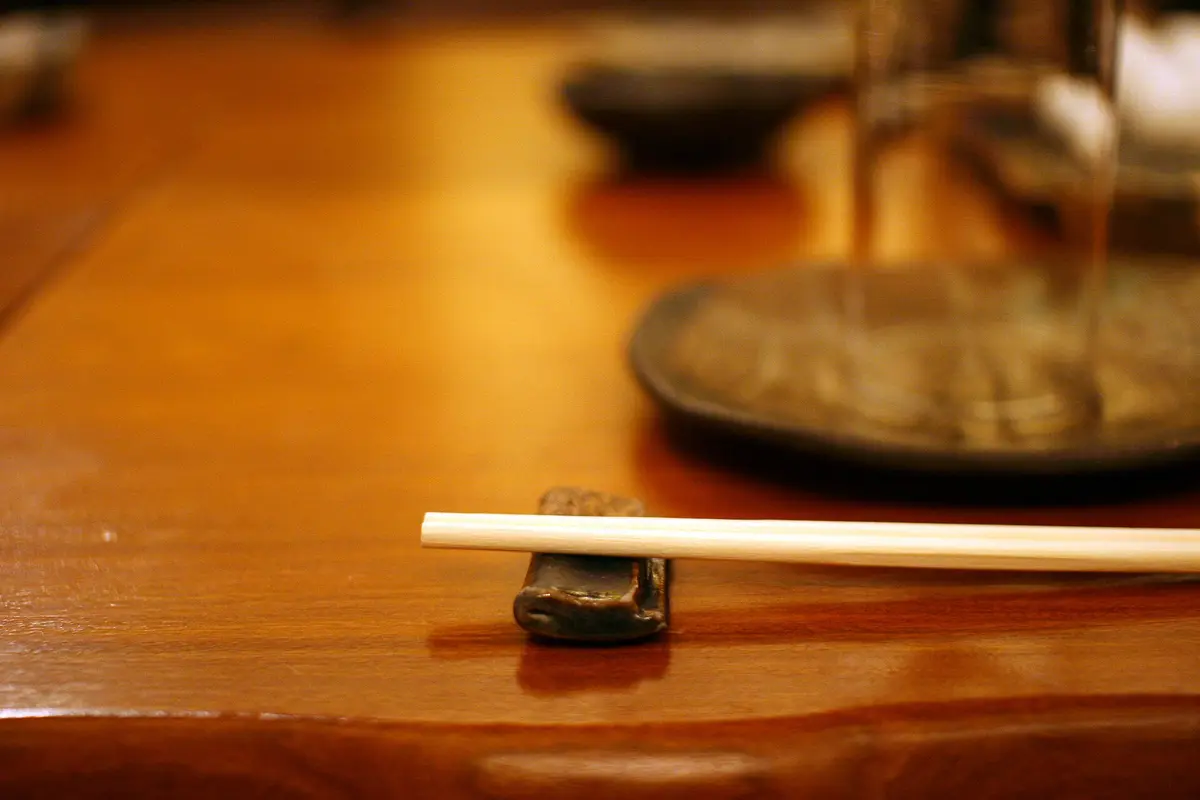 木桌上，一双筷子横放在小巧的陶制筷架上，后方是一只模糊的器皿