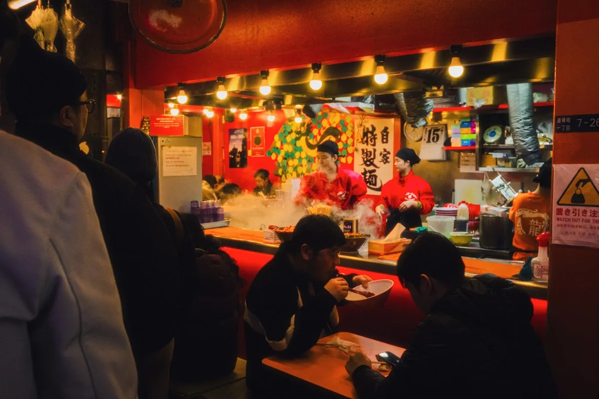 People eating at a busy Japanese street food stall with steam rising and warm lighting