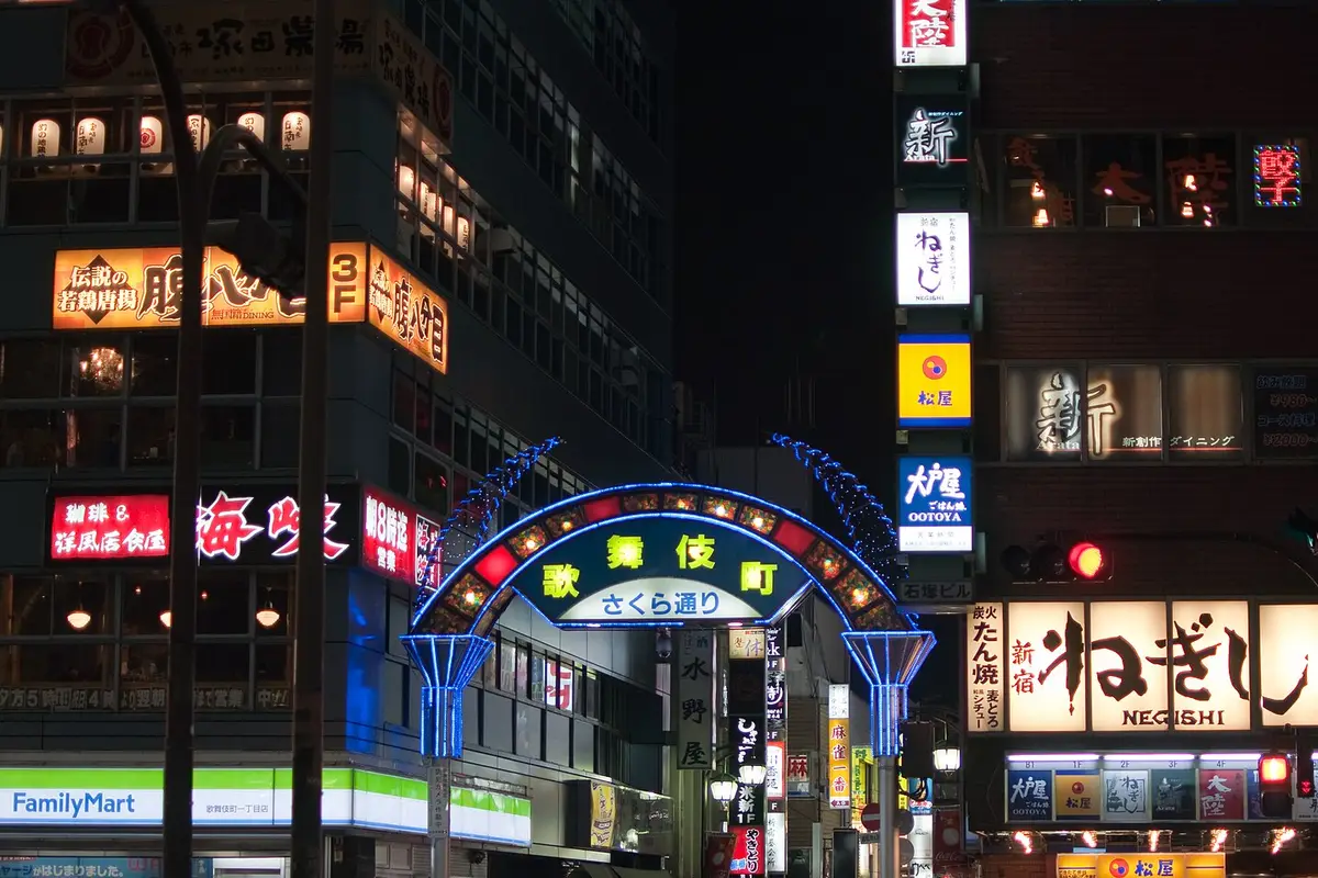 Kabukicho bei Nacht, auf Straßenhöhe: das beleuchtete Tor am Eingang zur Sakura-dori, zwischen den Schildern eines Convenience Stores und von Kettenrestaurants
