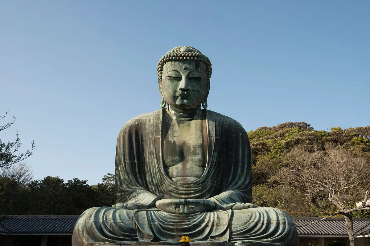 The bronze Great Buddha of Kamakura seated in the open air under a clear sky, with low temple roofs on either side