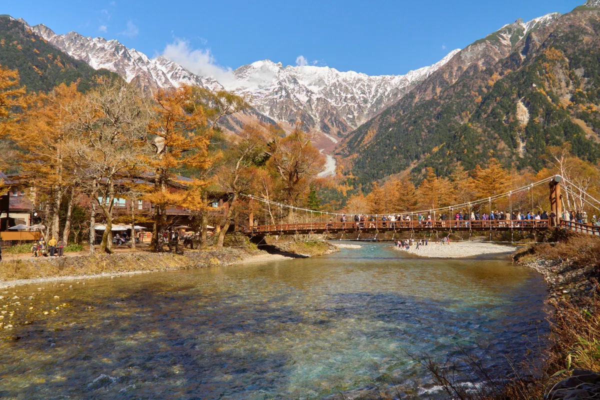 Snow-dusted Hotaka peaks above golden autumn larches, with the Azusa River and Kappa Bridge below in Kamikochi