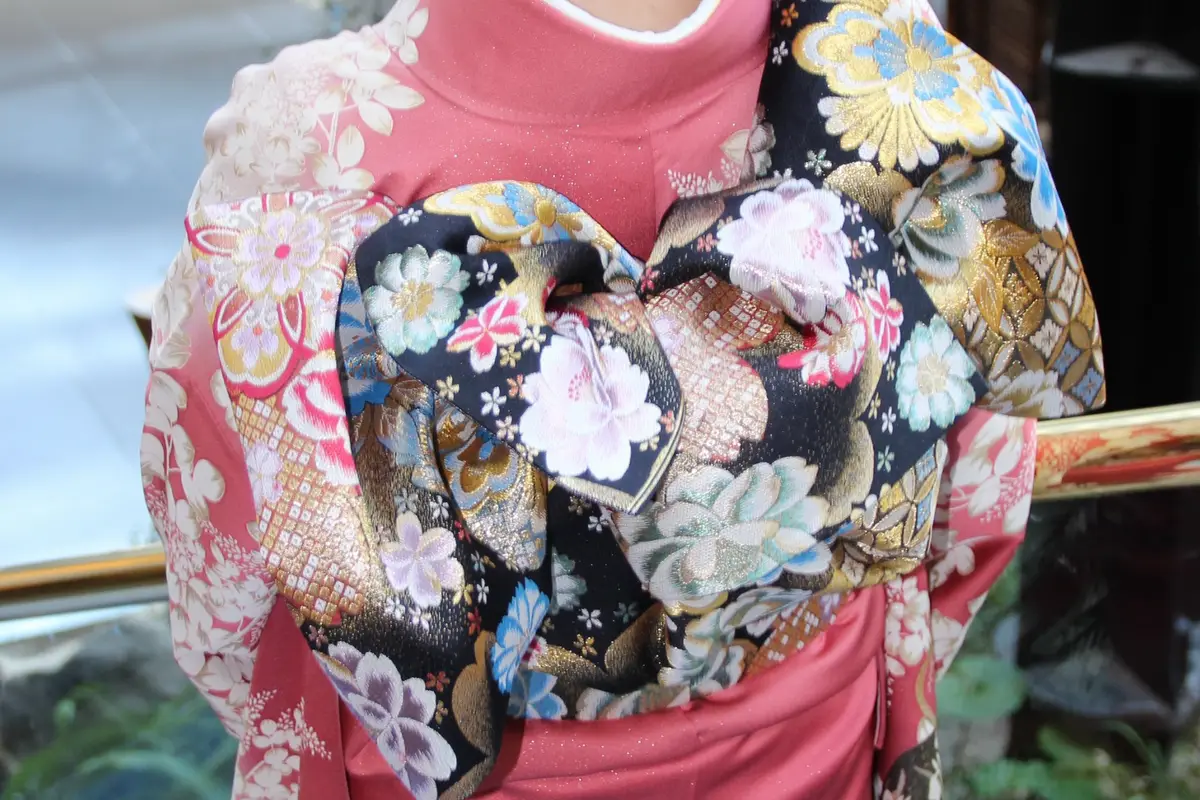 Close view of a patterned obi tied in a decorative bow at the back of a pink kimono
