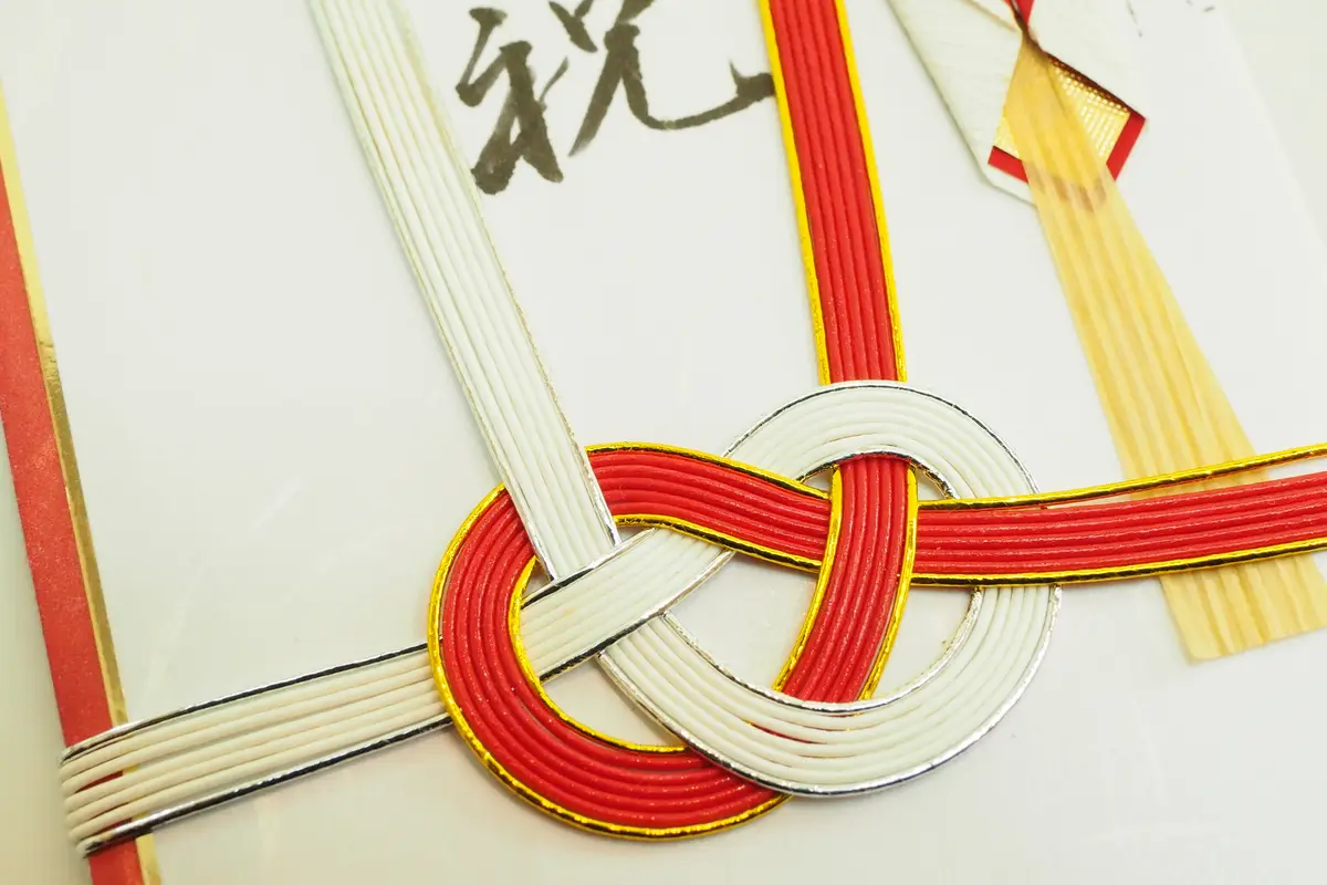 Close view of a red and white mizuhiki cord tied in a decorative knot across a white Japanese gift envelope