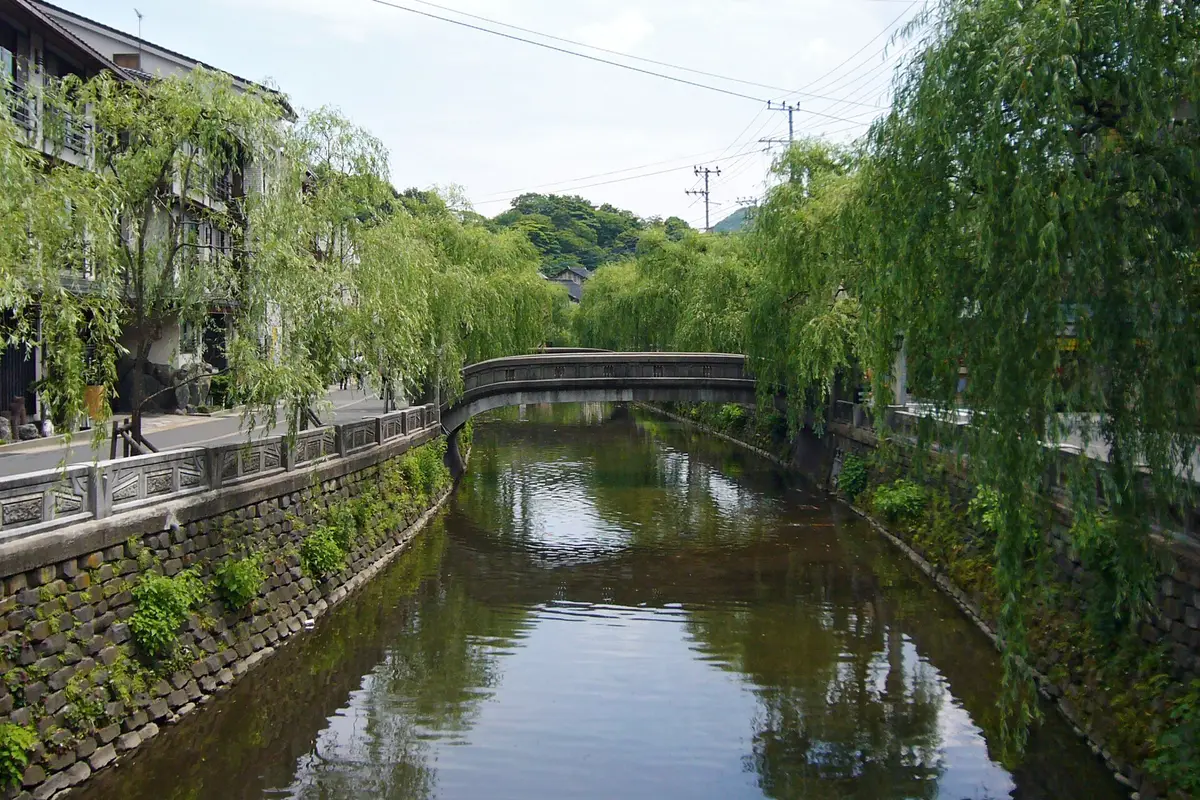 Willows lean over the canal running through Kinosaki Onsen, a low stone bridge arching across it and a stone balustrade lining the street along the bank