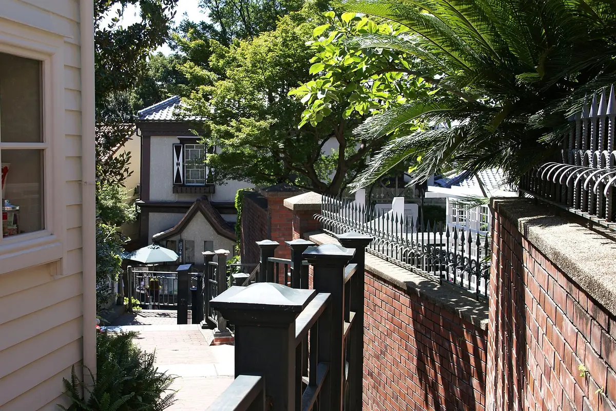 From the lane outside the gates: an old Western-style house in Kobe's Kitano district behind a brick wall and iron railings