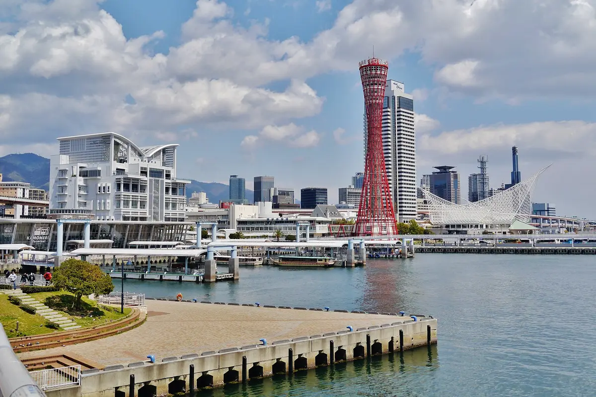 Seen from the quay: the red lattice of the Kobe Port Tower over Meriken Park, with the green hills standing behind the city