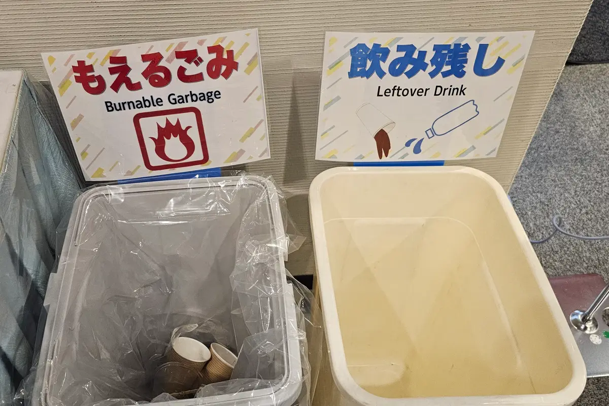 日本語と英語で「もえるごみ」「飲み残し」と書かれた札が立つ2つのゴミ箱。紙コップとペットボトルの中身を空ける絵が添えられている