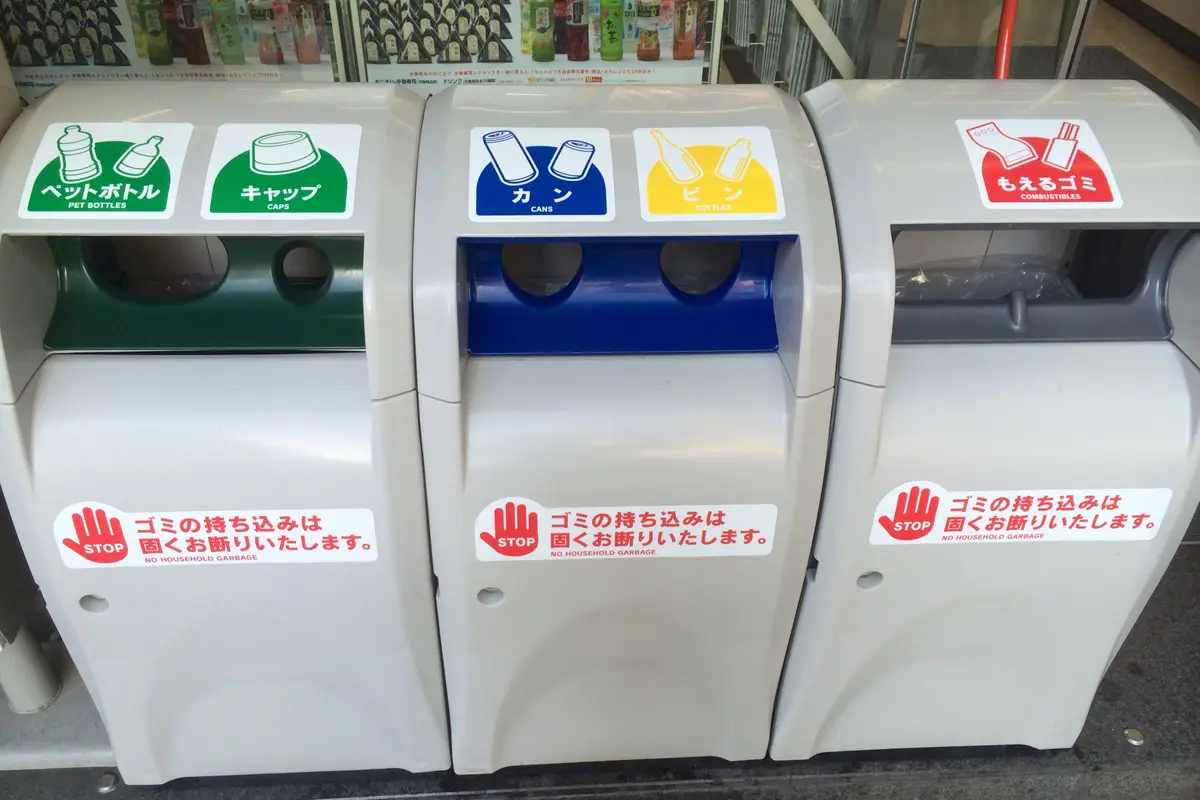 日本の店の前に並ぶ3台の分別ゴミ箱を近くから見たところ。ペットボトル、キャップ、缶、ビン、燃えるゴミの投入口にそれぞれ表示がついている