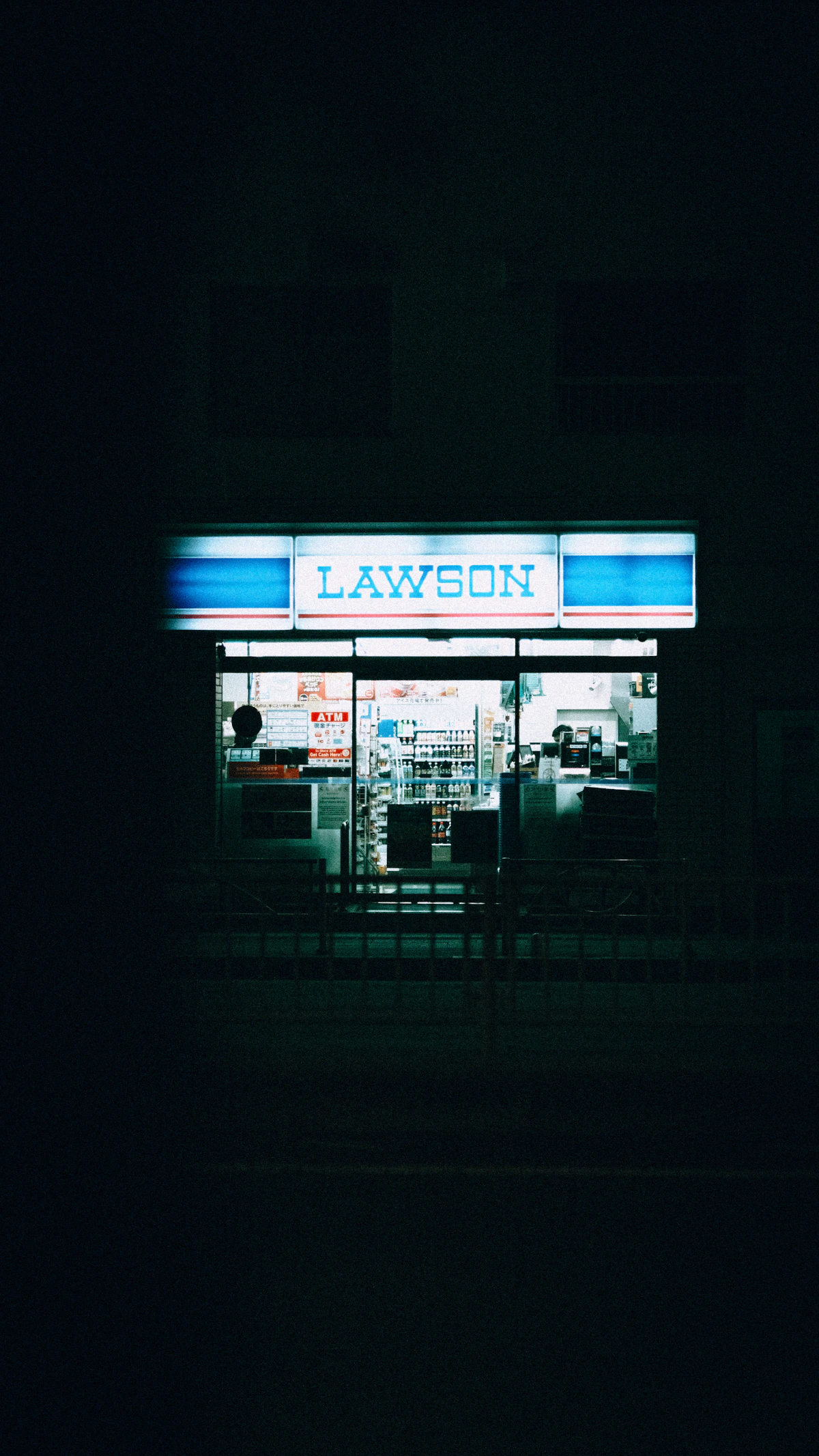 A Lawson convenience store glowing in the dark on a quiet Japanese street at night