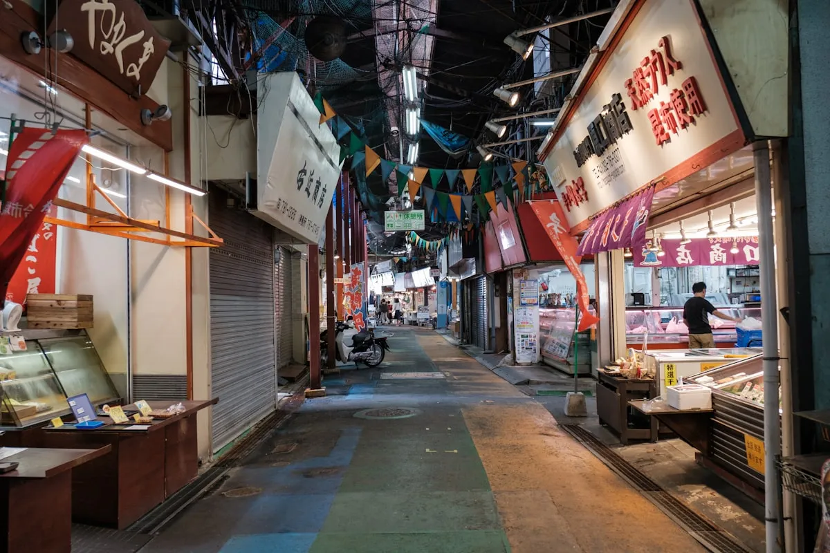 A quiet Japanese shotengai covered market street with local shops and colorful flags