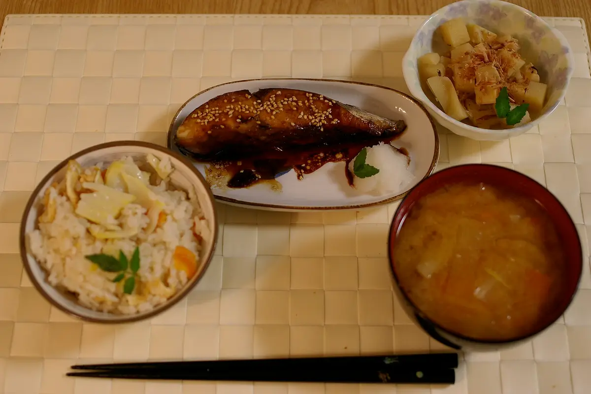 A Japanese home dinner seen from above: mixed rice, grilled fish with grated daikon, simmered bamboo shoots, and miso soup
