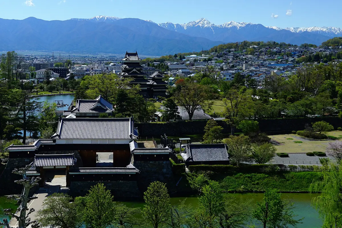 Looking down over the city of Matsumoto: the black keep among the trees of the castle park, with the snow-capped ridges of the Northern Alps along the skyline