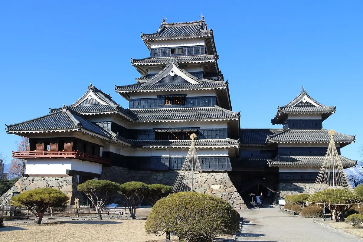 Seen from the castle grounds on a clear winter day: the black keep of Matsumoto Castle in tiers of dark boards and white plaster, with the red-railed moon-viewing turret to its left