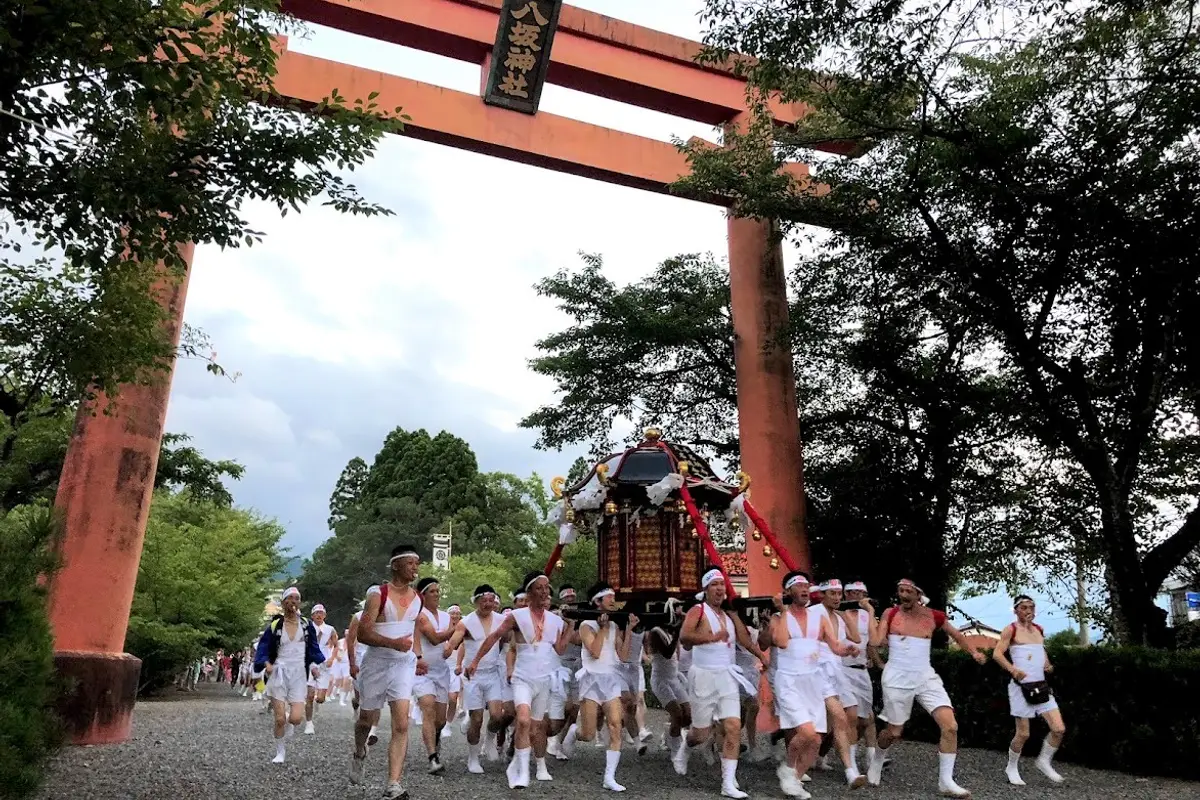 Seen from the shrine path: bearers in white carrying a mikoshi out through a large red torii gate