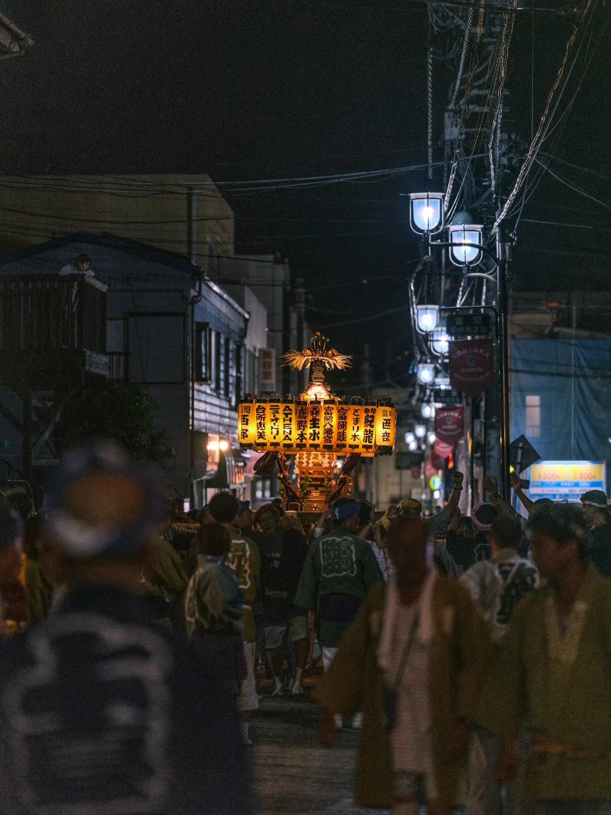 A golden mikoshi portable shrine lit with lanterns being carried through a narrow street at night