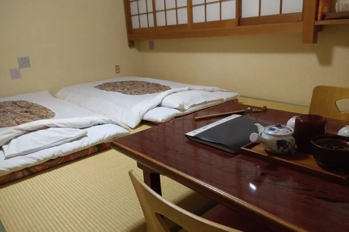 Two futons laid out on tatami mats in a ryokan guest room, with a teapot and cups on a low lacquered table