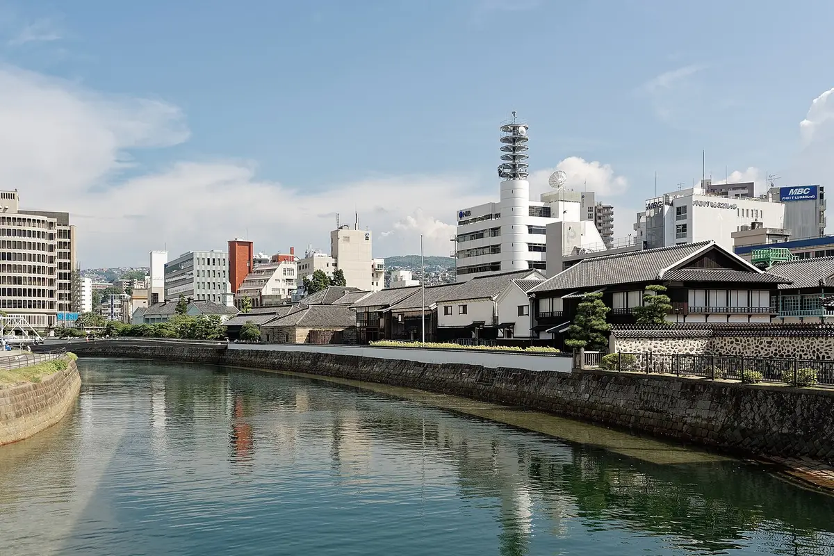 The rebuilt wooden buildings of Dejima on their stone seawall in central Nagasaki, with modern office towers standing directly behind them