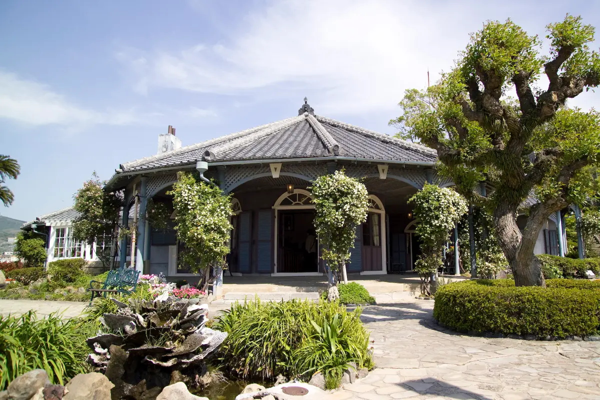 The former Glover residence at Glover Garden in Nagasaki, its wide veranda framed by flowering shrubs and a stone garden path