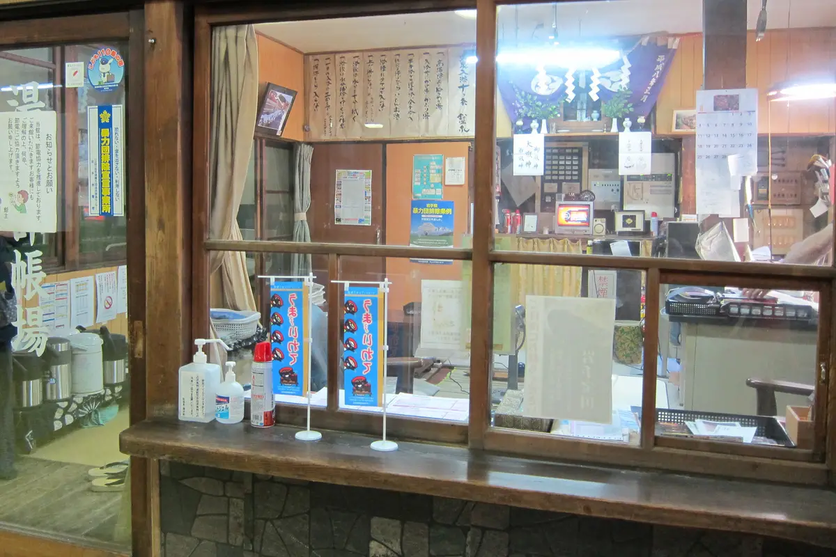 The reception window of an old Japanese inn, framed in dark wood, with handwritten notices posted inside