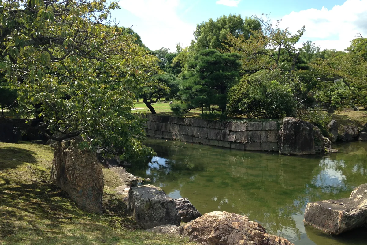 Quiet pond and stone-walled moat inside the Ninomaru Garden at Nijo Castle, framed by pine and cherry trees