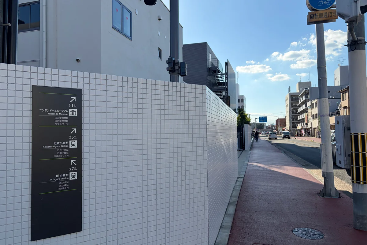 A directional sign in English and Japanese pointing toward the Nintendo Museum, one minute's walk away, on an ordinary residential street in Uji