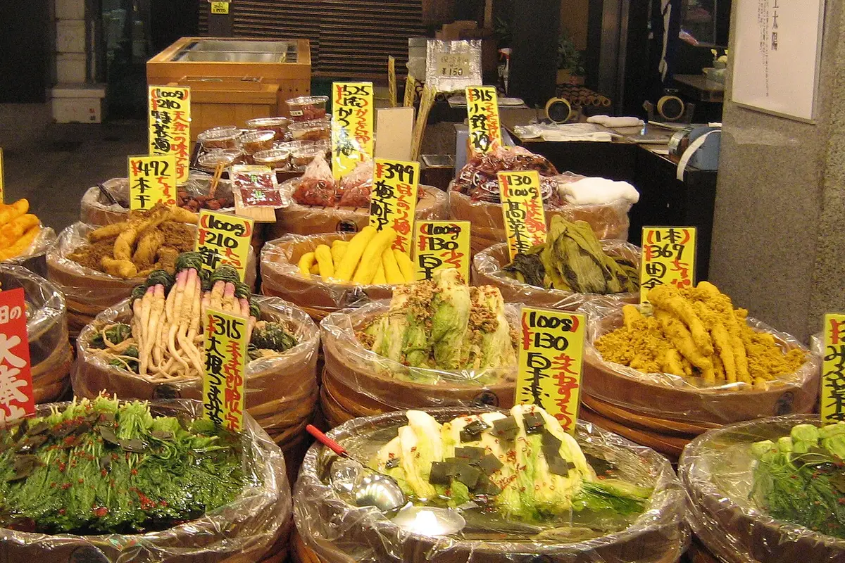 แถวถังไม้ใส่ผักดองเกียวโตที่หน้าร้านในตลาดนิชิกิ แต่ละถังมีป้ายเขียนมือบอกราคาตามน้ำหนัก