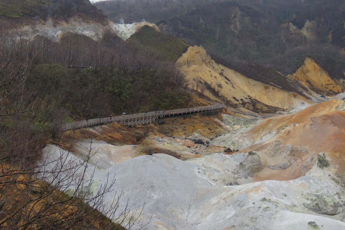 A wooden boardwalk crossing the bare, mineral-streaked crater floor of Noboribetsu Jigokudani