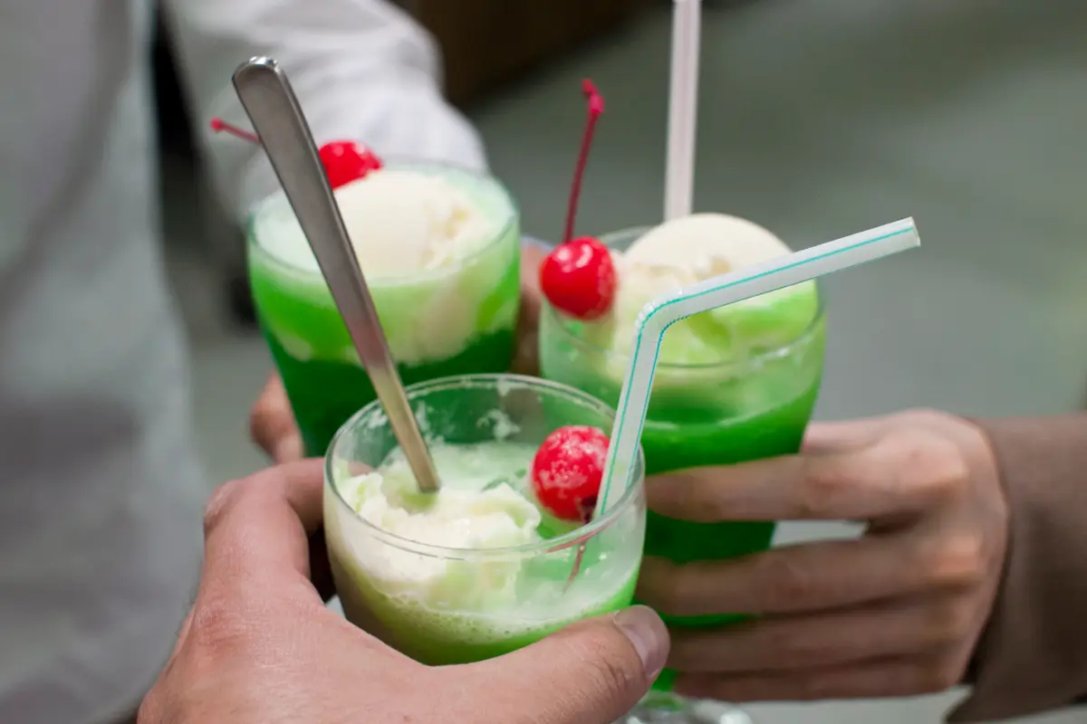 Three hands holding glasses of melon cream soda raised together in a toast