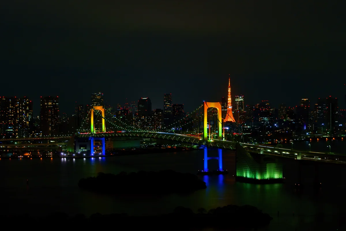The Rainbow Bridge illuminated at night, seen across the water from Odaiba's waterfront promenade