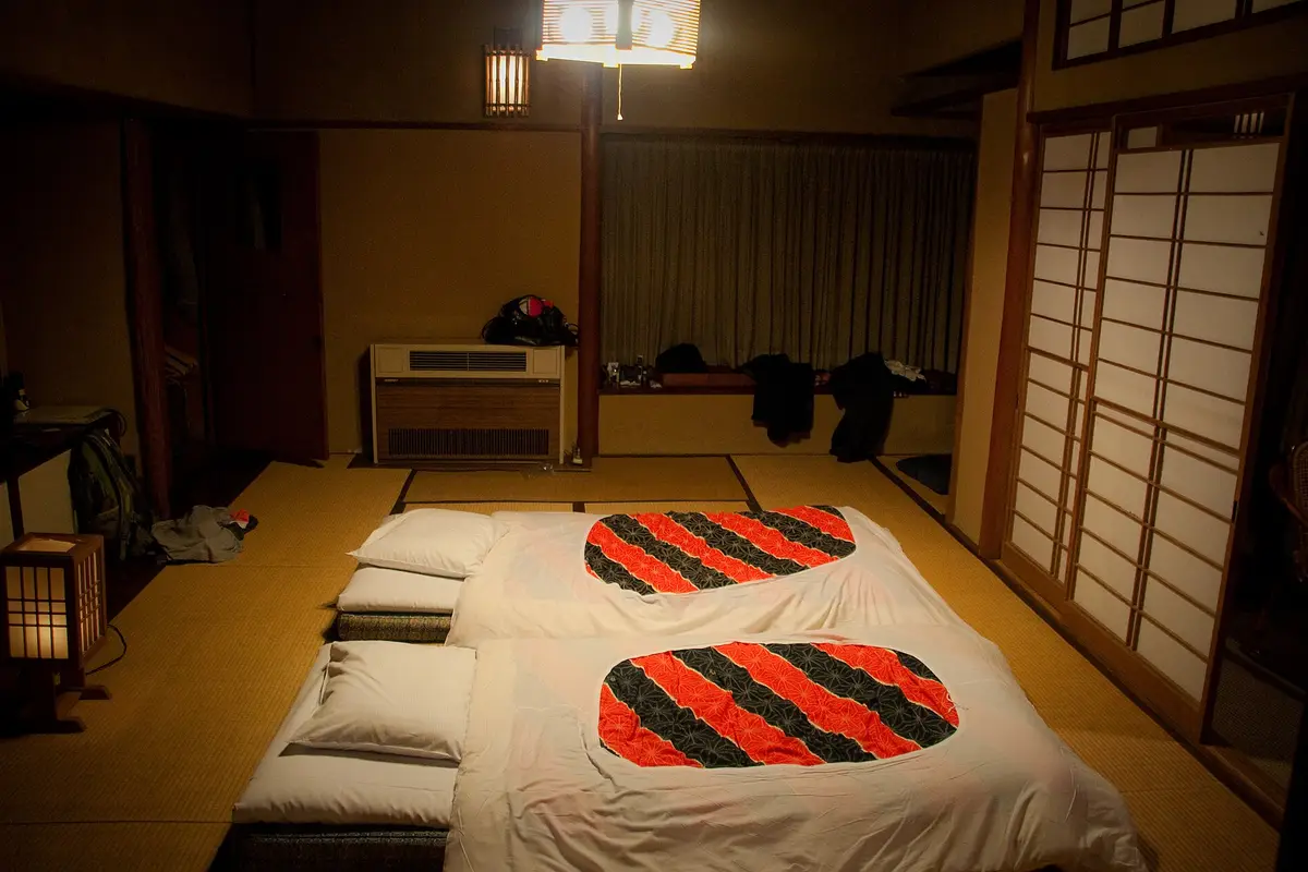 Two futons made up on the tatami of a ryokan room at night, under a paper lamp, with a shoji screen along one wall