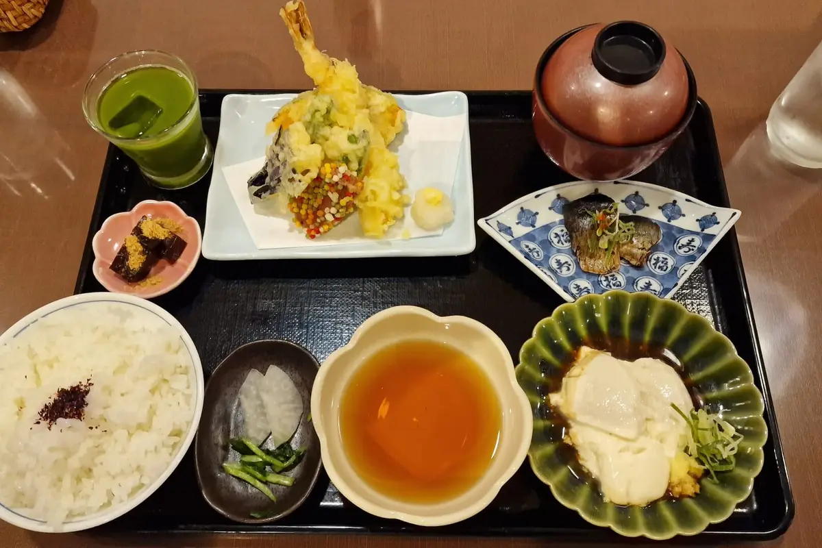 A Japanese set meal on a black lacquer tray: rice, tempura, grilled fish, pickles, a covered soup bowl and a dish of tofu, each served in its own vessel