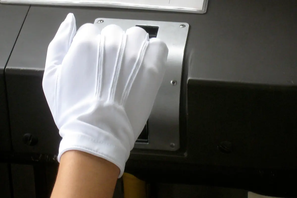 A hand in a white uniform glove gripping a recessed metal handle on a dark panel, photographed close up