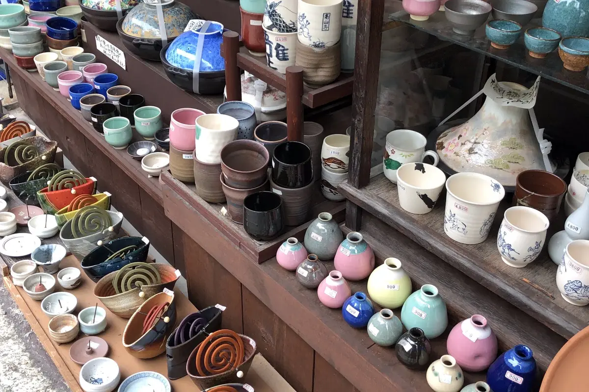 Tiered outdoor shelves at a pottery shop in Kyoto, filled with cups, bowls and small vases, each carrying a small printed price sticker