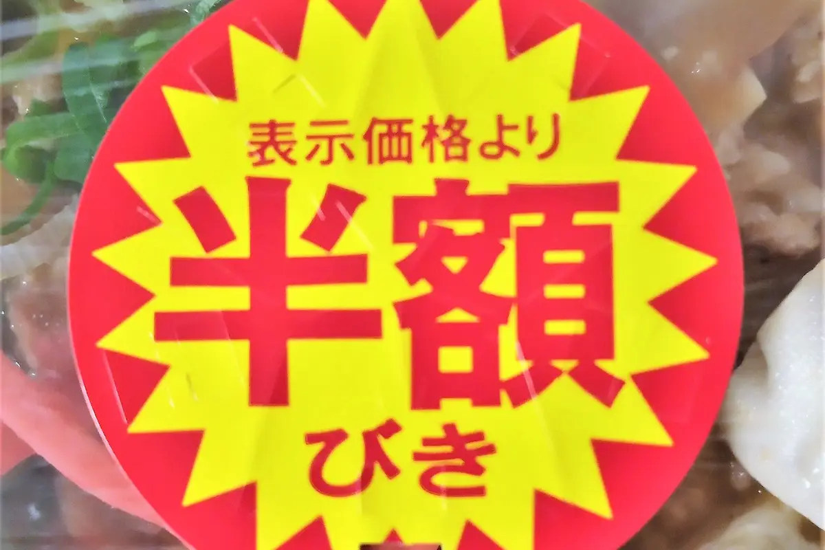 A large red and yellow discount sticker covering the lid of a packed supermarket meal, with the food visible around its edges