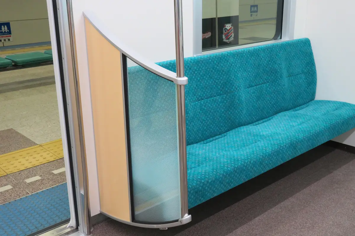 An empty teal priority seat bench beside the door of a Sapporo Municipal Subway car, with the station platform visible through the open doorway