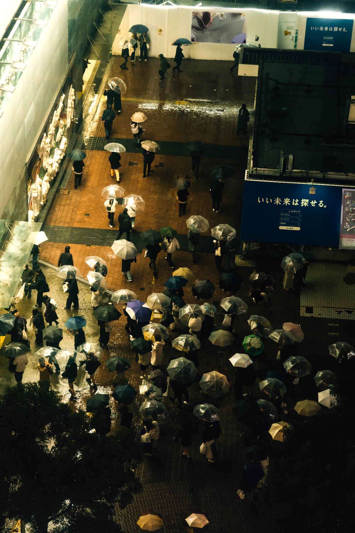 An aerial view of people navigating a rainy Japanese street with umbrellas